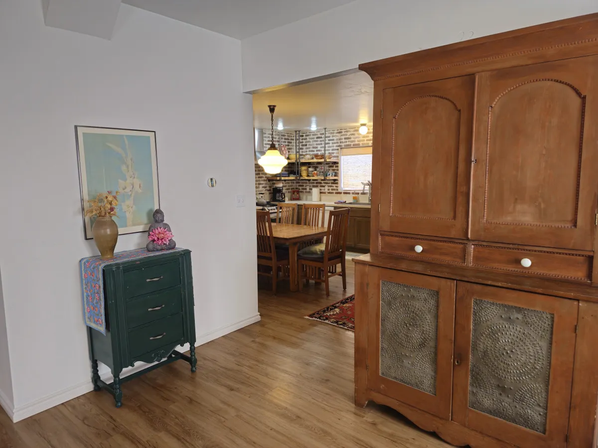 A warm living space with a green dresser, wooden cabinet, and framed artwork, with a glimpse into a dining area in the background. The setup is perfect for entertaining guests and hosting shared experiences.