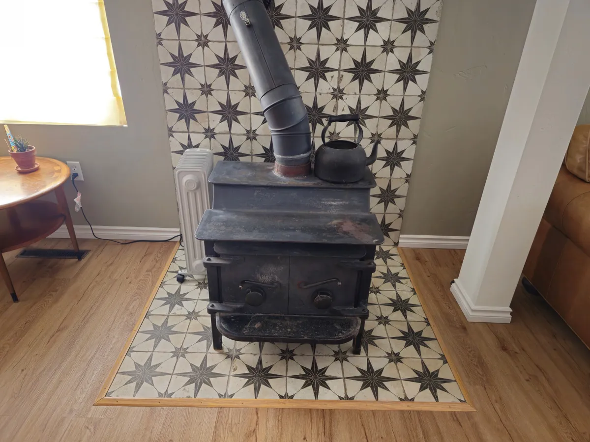 A cozy corner with a wood-burning stove, decorative tiles, a small wooden table, and a kettle. The warm glow of the stove creates an inviting atmosphere, ideal for unwinding after a cold day on the slopes. The scene captures the essence of returning home to comfort and warmth.