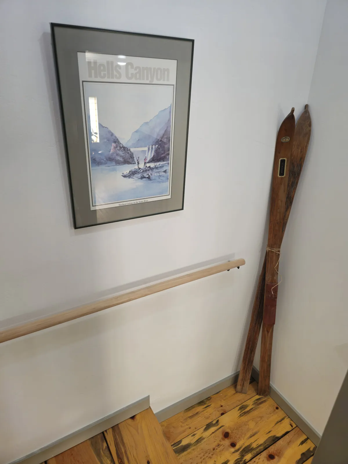 This image features a framed artwork of Hells Canyon and a set of vintage wooden skis displayed on a wooden railing and textured floor. The scene is nostalgic and evokes a sense of outdoor adventure, with the skis serving as a visual nod to the region's vibrant skiing culture. The setting encourages conversation and planning around mountain activities.