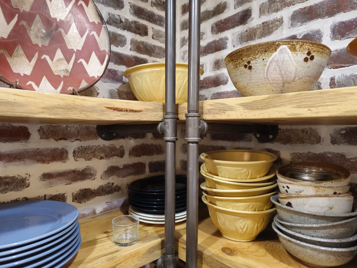 A close-up view of rustic wooden shelves packed with handcrafted bowls and colorful plates, suggesting family gatherings, festive meals, and entertaining. The arrangement highlights both aesthetic appeal and functional warmth.