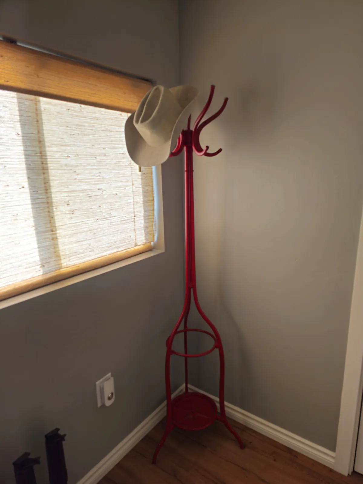 A casual entry area featuring a red coat rack with a cowboy hat, a window filtering in natural light, and a welcoming atmosphere. The scene evokes the ritual of coming home after outdoor pursuits.