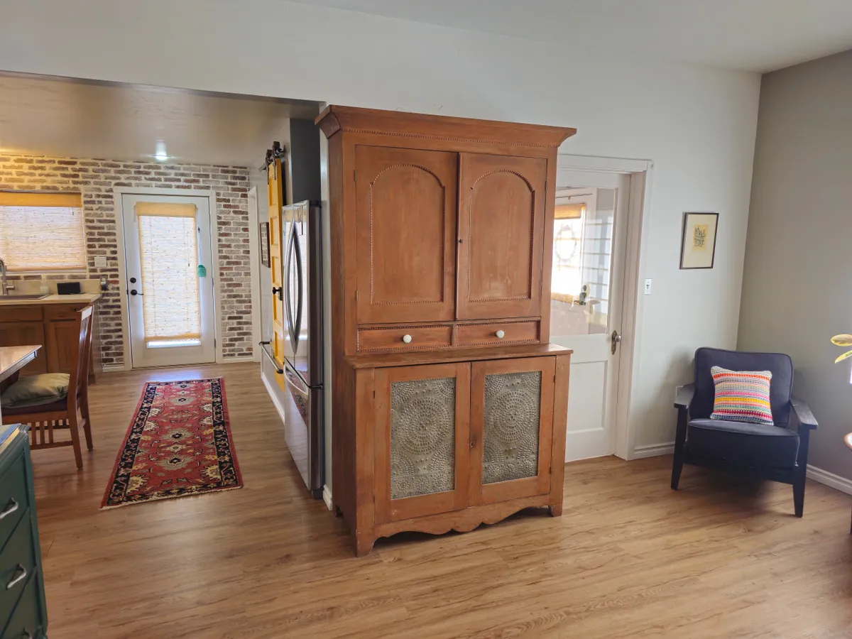 A warm kitchen scene with a wooden armoire, exposed brick wall, and an armchair set atop a cozy rug. The space feels inviting—ideal for gathering, cooking, or sharing a meal after a day spent exploring the area.