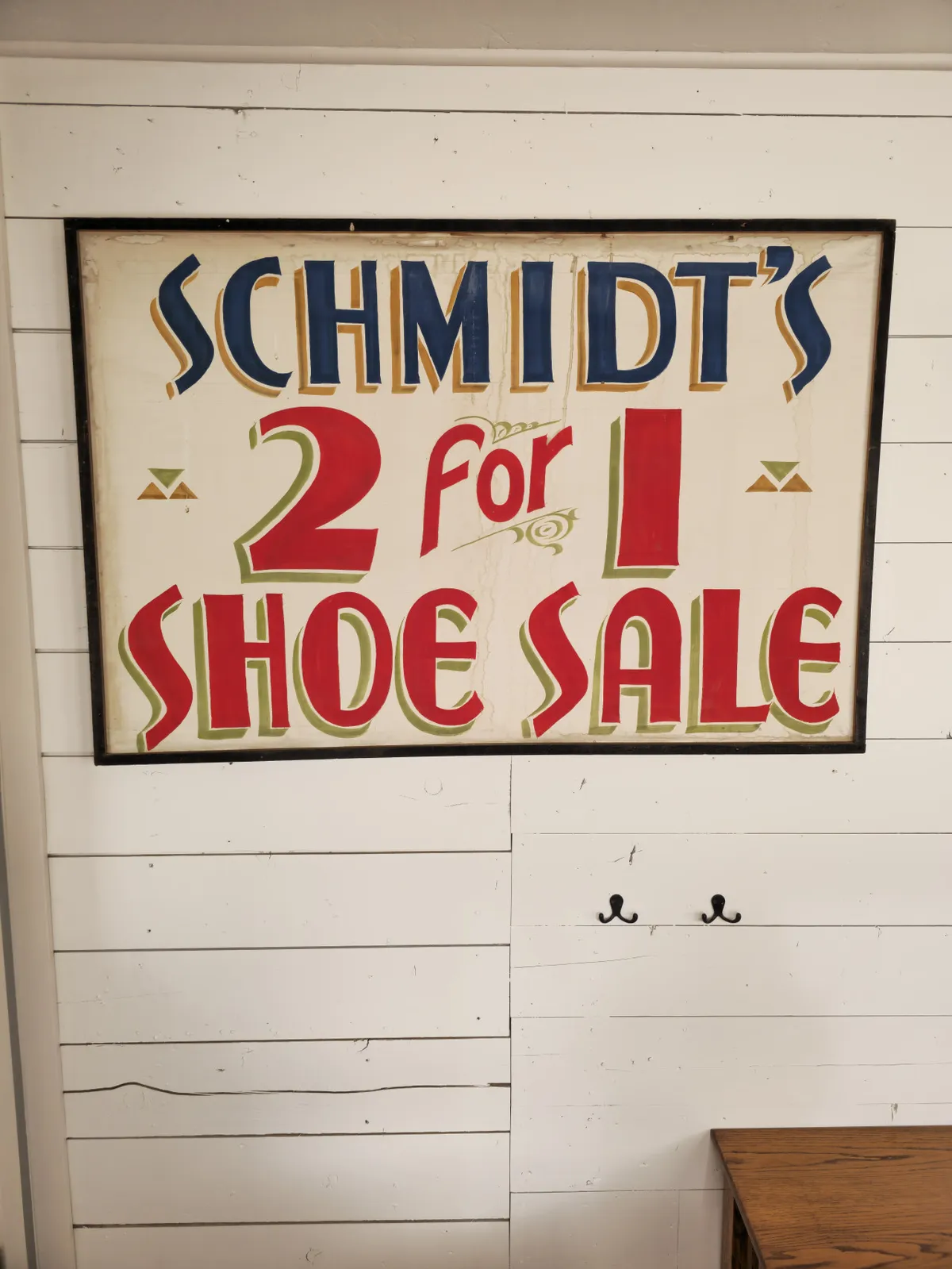A vignette of a vintage sign on a white wooden wall above a rustic wooden table, reminiscent of local shops or a classic Americana setting. The cheerful, inviting mood reflects a sense of exploration and discovery.